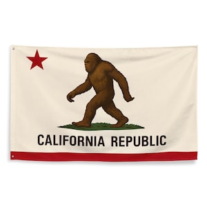 May include: A California Republic flag featuring a brown Bigfoot walking on green grass. The flag has a red star in the upper left corner and a red stripe at the bottom. The words "CALIFORNIA REPUBLIC" are printed in black.