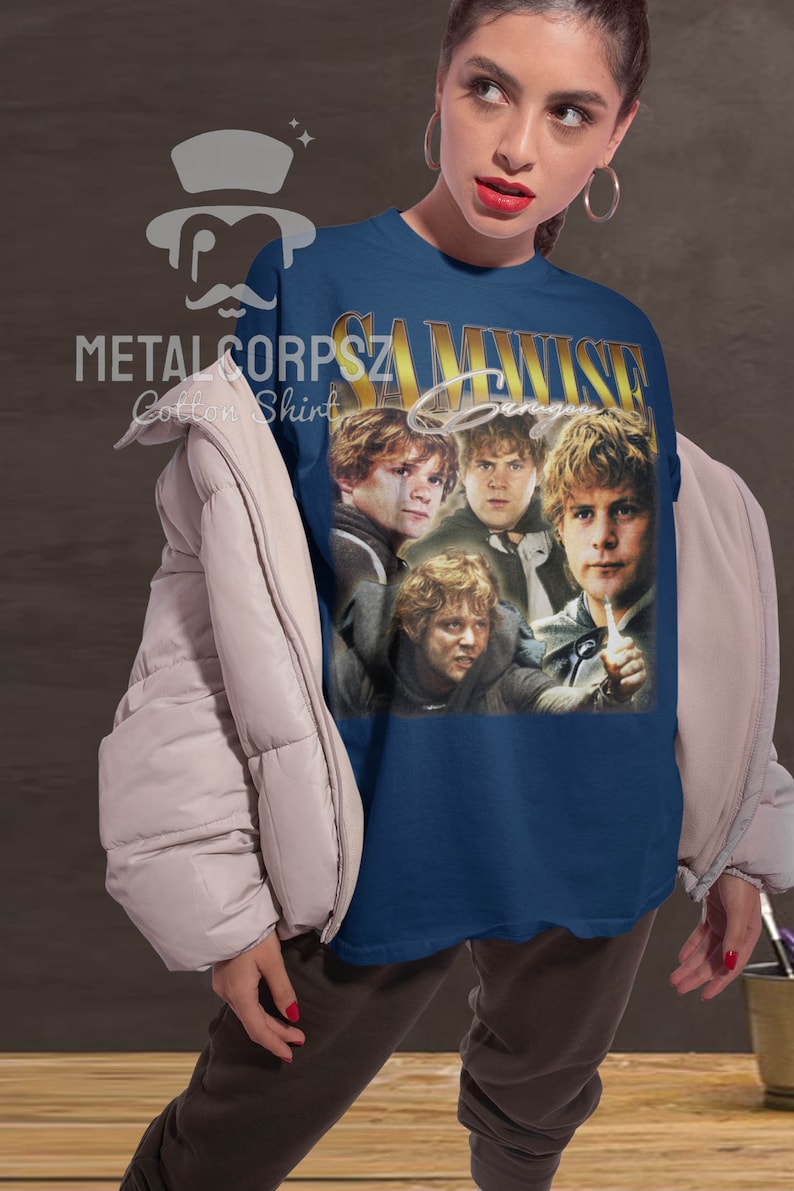 May include: A navy blue t-shirt with a vintage-style graphic of Samwise Gamgee from the Lord of the Rings. The graphic features four images of Samwise Gamgee in different poses. The text "SAMWISE GAMGEE" is printed in gold letters above the graphic.