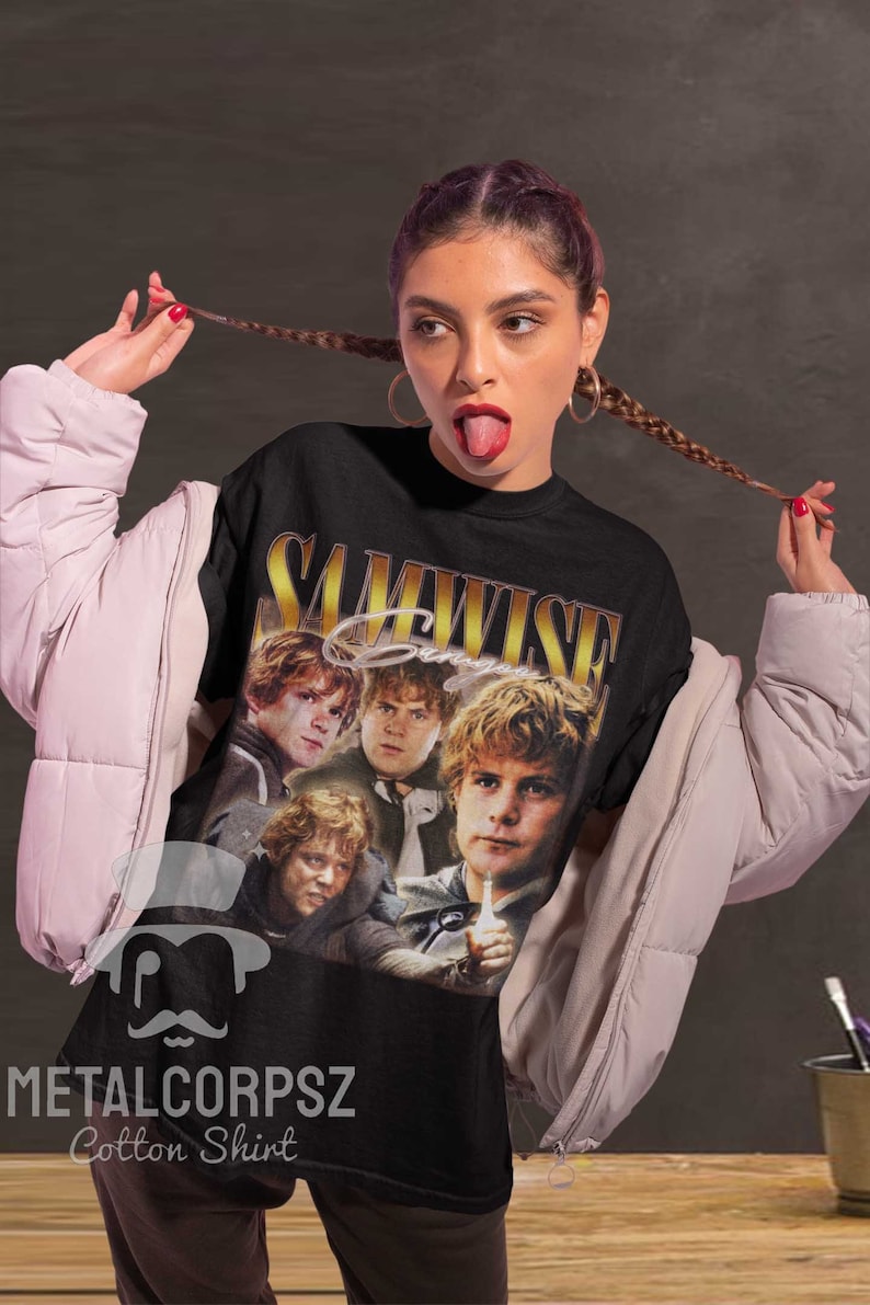 May include: Black cotton t-shirt with a vintage-style graphic of four characters from the Lord of the Rings movie. The graphic features the text "Samwise Gamgee" in gold lettering. The shirt has the text "METALCORPSZ Cotton Shirt" printed on the bottom.