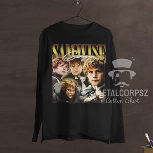 May include: Black long-sleeve t-shirt with a vintage-style graphic of Samwise Gamgee from the Lord of the Rings. The graphic features multiple images of Samwise in different poses, with the text "SAMWISE" in gold lettering above the images. The text "METALCORPSZ Cotton Shirt" is printed in white below the graphic.