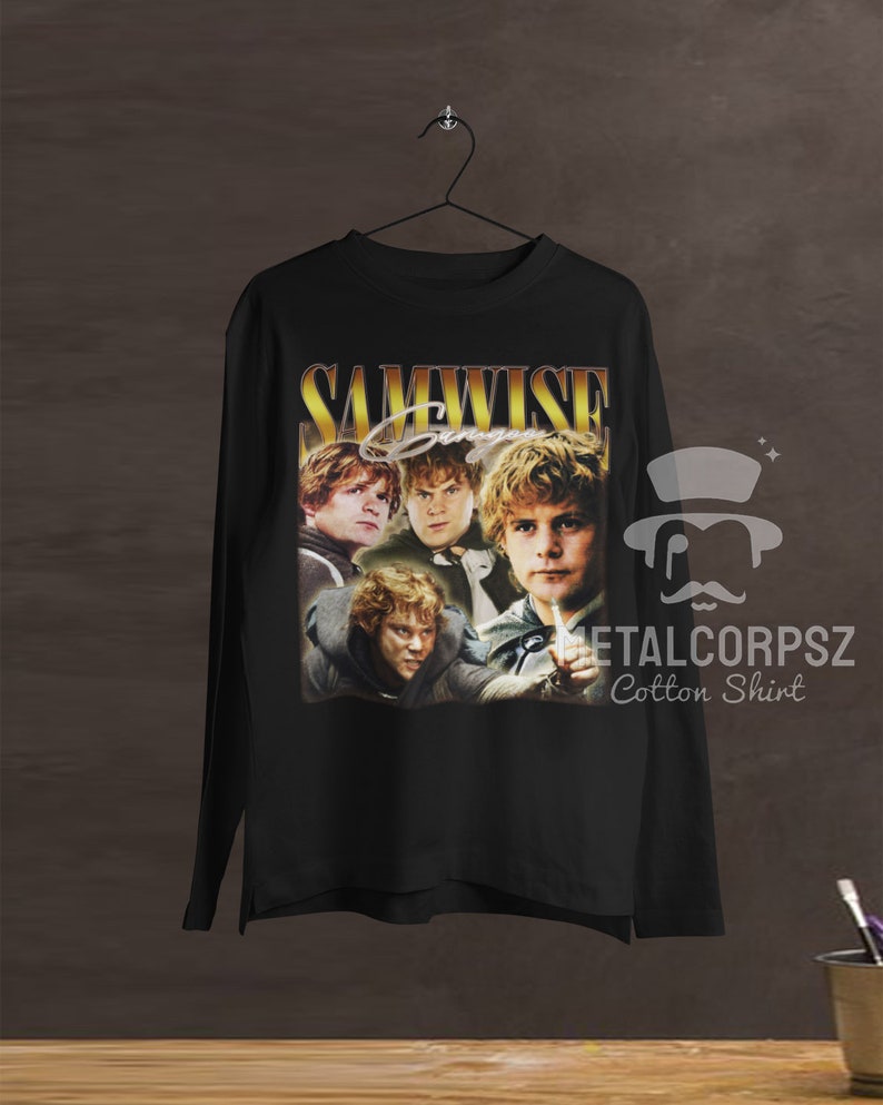 May include: Black long-sleeve t-shirt with a vintage-style graphic of Samwise Gamgee from the Lord of the Rings. The graphic features multiple images of Samwise in different poses, with the text "SAMWISE" in gold lettering above the images. The text "METALCORPSZ Cotton Shirt" is printed in white below the graphic.
