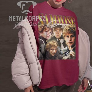 May include: A maroon t-shirt with a vintage-style graphic of Samwise Gamgee from the Lord of the Rings. The graphic features four images of Samwise Gamgee in different poses. The text "Samwise Gamgee" is printed in gold letters above the graphic.