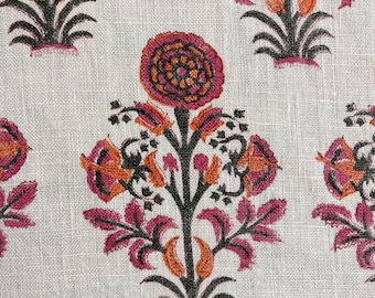 Op de afbeelding: Een witte stof met een herhalend patroon van roze, oranje en zwarte bloemenontwerpen. De bloemen zijn gestileerd en hebben een traditionele Indiase uitstraling.