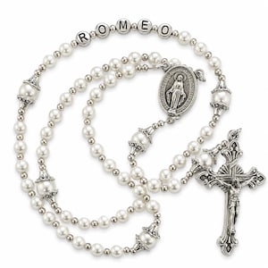 May include: A rosary featuring white pearl beads, silver-toned metal spacers, and a crucifix. The beads spell out the name ROMEO in silver-toned letter blocks. An oval-shaped medal depicting a figure is attached to the chain near the crucifix.