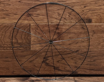 May include: A black metal wreath frame with a circular shape and spokes radiating from the center.