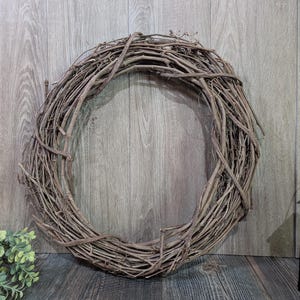 May include: A circular wreath constructed from intertwined brown natural twigs and branches. The wreath features a hollow center and a textured, organic appearance with varying thicknesses of wood throughout the circular frame structure.