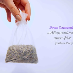 May include: A clear plastic bag filled with dried lavender buds. The bag is held by a hand against a white background. Text in the image reads "Free Lavender with purchases over $35 (before Tax)".