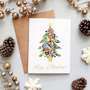 May include: A white Christmas card with a gold foil design of a Christmas tree decorated with colorful flowers and the text "Merry Christmas".