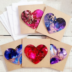 May include: Set of six blank greeting cards featuring abstract heart designs in shades of pink, purple, and blue. Each card is made of thick paper and has a white envelope.