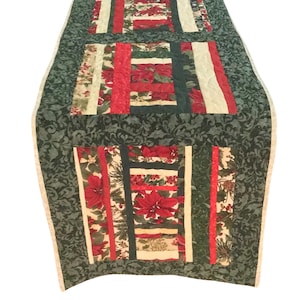 Op de afbeelding: Een groene gestikte tafelrunner met een kerstthema. De runner heeft een patchwork-ontwerp met rode, groene en witte stoffen. De stoffen hebben een bloemenpatroon met kerststerren en hulst.