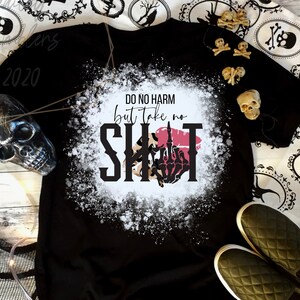 Może przedstawiać: Czarny t-shirt z napisem "DO NO HARM but take no SHIT" w czarno-białym wzorze. Projekt zawiera szkielet dłoni i czerwone usta. Koszulka otoczona jest dekoracjami na Halloween.