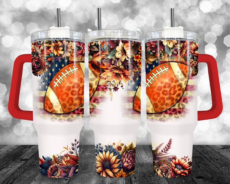 May include: Three white insulated tumblers with a football and floral design. The design includes an American flag, a football with a leopard print pattern, and colorful flowers. Each tumbler has a red handle and a silver straw.
