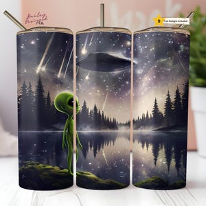 May include: A set of three stainless steel tumblers with a design of a green alien looking up at a flying saucer in a starry night sky. The tumblers are surrounded by a forest and a lake.