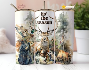 Puede incluir: Tres vasos de acero inoxidable con un diseño de acuarela de una escena de bosque. El vaso del centro presenta un ciervo con cuernos y el texto "tis' the season". El vaso de la izquierda presenta un oso, un pato y un perro. El vaso de la derecha presenta un alce y un mapache.