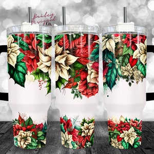 May include: A white stainless steel tumbler with a black handle and a lid. The tumbler features a Christmas-themed design with red and white poinsettia flowers, green leaves, and red berries.
