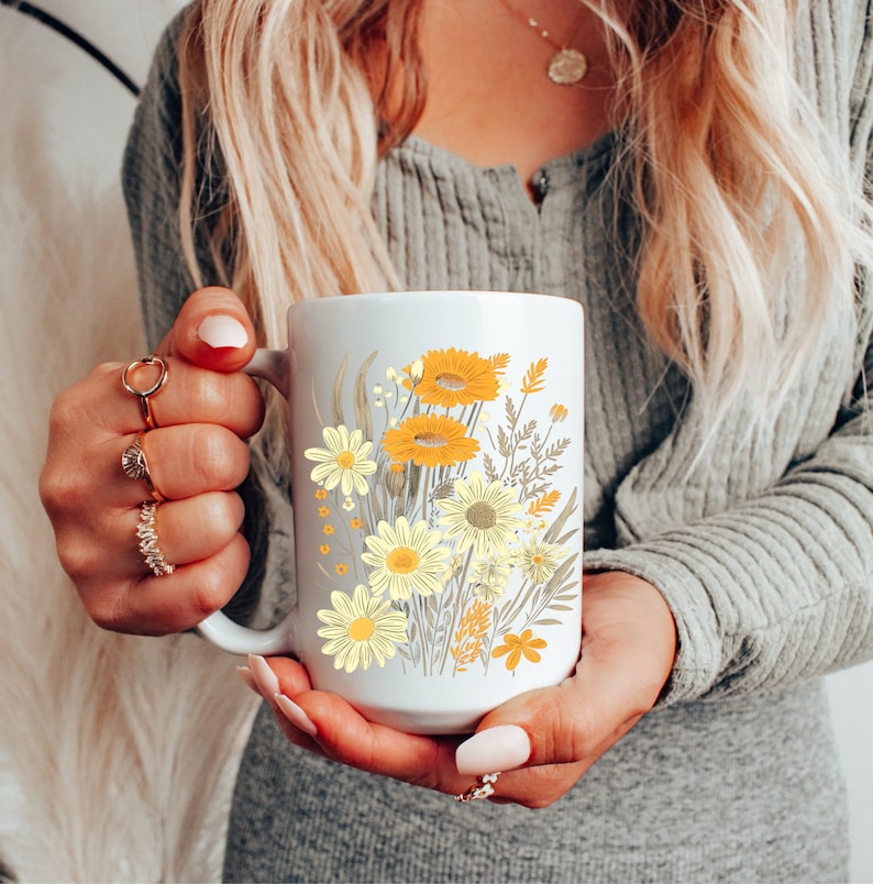 May include: White ceramic mug with a floral design featuring yellow and orange flowers on a white background.