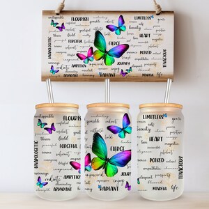 Puede incluir: Tres vasos de vidrio transparente con tapas de bambú y pajitas de metal. Cada vaso presenta un gráfico de mariposa colorido y una lista de palabras positivas, que incluyen "Limitless", "Flourish" y "Radiant".