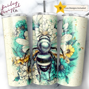 May include: A set of three stainless steel insulated tumblers with a bee and floral design. The design features a large bee with white wings, surrounded by teal, yellow, and white flowers. The tumblers have a cream-colored background with gold speckles. The text "9 Free Designs Included" is visible.