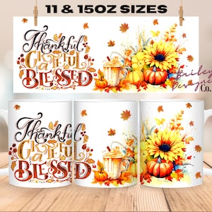 May include: Two white ceramic mugs with a fall-themed design. The mugs feature a sunflower, pumpkins, and leaves in shades of orange, yellow, and brown. The text "Thankful Grateful Blessed" is written in a decorative font on the mugs.