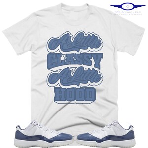 May include: White t-shirt with the text "A Little Classy A Little Hood" in blue lettering. The shirt is paired with a pair of white and blue sneakers.
