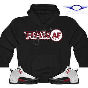 Puede incluir: Sudadera negra con un gr&aacute;fico "RAW AF" rojo y blanco y un par de zapatillas blancas y negras con detalles rojos.