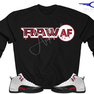 Puede incluir: Sudadera negra con el texto "RAW AF" en rojo con detalles blancos que gotean. La sudadera se combina con zapatillas blancas y negras con detalles rojos.