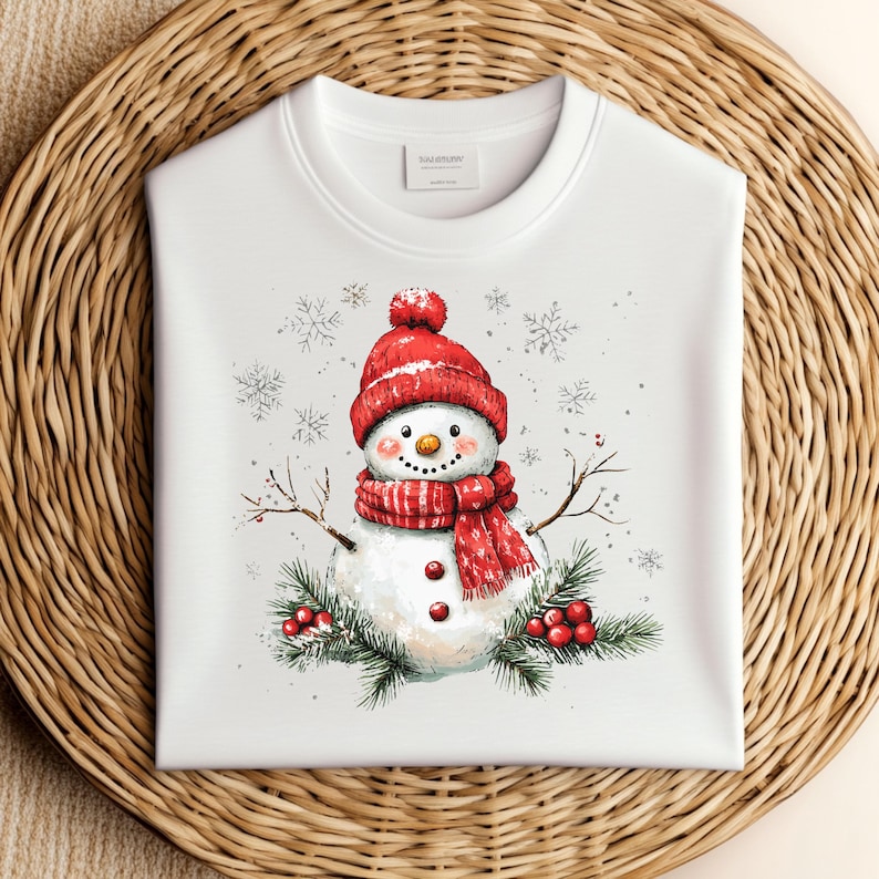 Puede incluir: Sudadera blanca con una ilustraci&oacute;n de un mu&ntilde;eco de nieve rojo y blanco. El mu&ntilde;eco de nieve lleva un gorro rojo con un pomp&oacute;n blanco y una bufanda a rayas rojas y blancas. El mu&ntilde;eco de nieve est&aacute; rodeado de copos de nieve y ramas de pino con bayas rojas.