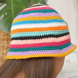 May include: A colorful striped crochet bucket hat with a yellow brim. The hat is made with a variety of colors, including pink, orange, teal, purple, and black.