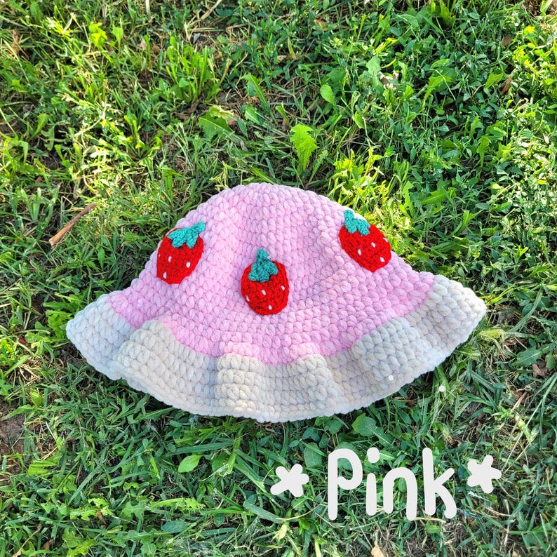 K&ouml;nnte beinhalten: Rosa gestrickter Bucket-Hut mit wei&szlig;em Rand und drei gestickten Erdbeer-Designs.