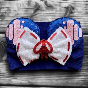 May include: A blue headband with a white and red bow and blue and pink sequined ears.