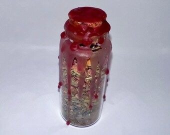 May include: A glass jar filled with dried herbs and flowers, sealed with a red wax cork. The wax has dripped down the sides of the jar, creating a decorative effect.