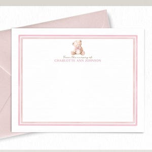 May include: Blush pink stationery set featuring a teddy bear illustration. The set includes a card with a double pink border and the text "From the nursery of CHARLOTTE ANN JOHNSON", and a matching envelope.
