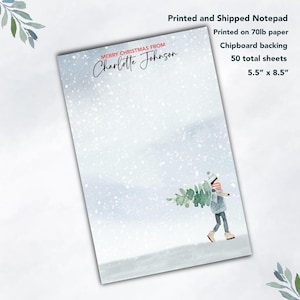 May include: A personalized notepad with a winter scene featuring a person carrying a Christmas tree in the snow. The notepad is printed on 70lb paper with a chipboard backing and has 50 total sheets. It measures 5.5 inches by 8.5 inches. The text on the notepad reads "Merry Christmas from Charlotte Johnson".