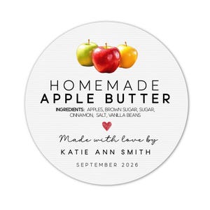 May include: A round white label with the text "HOMEMADE APPLE BUTTER" and the ingredients listed below. The label features three apples: green, red, and yellow. The text "Made with love by KATIE ANN SMITH SEPTEMBER 2026" is also included.