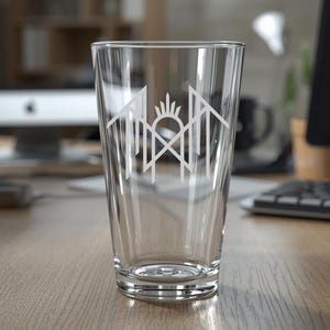 A clear glass with a white logo on it, placed on a wooden desk in an office setting.