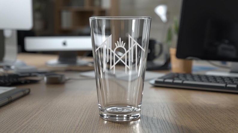 A clear glass with a white logo on it, placed on a wooden desk in an office setting.
