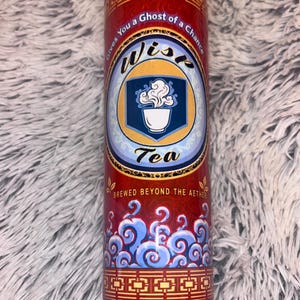 May include: Red tumbler with the text "Gives You a Ghost of a Chance" and "Wisp Tea." The design includes a blue and white logo of a teacup with steam, and blue cloud-like patterns. The tumbler is cylindrical.