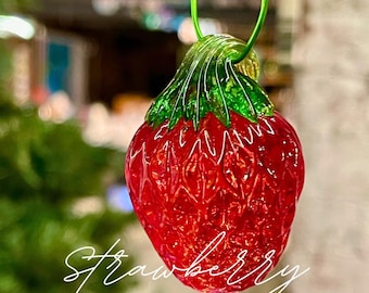 May include: A red glass strawberry ornament with a green glass stem and leaves. The ornament is hanging from a wire loop.