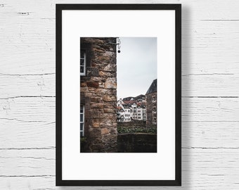 Pode incluir: Uma fotografia emoldurada de um edifício de pedra com vista para outros edifícios à distância. O edifício de pedra está em foco, e os outros edifícios estão fora de foco.