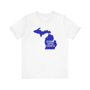 May include: White t-shirt featuring a blue outline of the state of Michigan. The words "EVERY VOTE COUNTS" are printed in blue within the lower peninsula of the state. The shirt is made of a soft material.