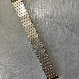 May include: A silver metal watch band with a curved end. The band is made of many small, linked pieces.