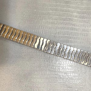 May include: A silver and gold metal watch band with a wave-like pattern.