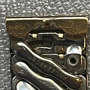 May include: Close-up of a gold and silver watch band with the inscription "2010KG" and the numbers "24.52306".