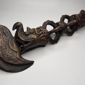 May include: Bronze-colored ritual blade with intricate dragon and floral designs. The blade has a curved edge and is connected to a handle with a series of looped elements. The handle ends with a bird-like figure.