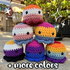 May include: A stack of six crocheted octopus plushies in various color combinations, including pink, white, blue, orange, yellow, and purple. The plushies are arranged in a pyramid shape, with the largest plushie at the top and the smallest plushie at the bottom. The plushies have black eyes and are made with a soft, textured yarn. The text " + more colors" is written below the plushies.
