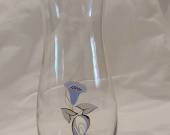 May include: A clear glass vase with a blue and gold floral design. The vase has a wide base and a narrow neck.
