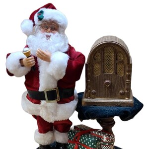 May include: A Christmas-themed figurine of Santa Claus holding a microphone, dressed in a red suit with white trim. Beside him is a vintage-style radio and wrapped gifts. The base is dark with text.