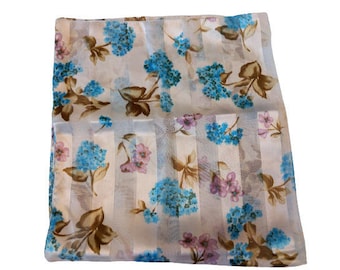 May include: A sheer white scarf with a floral pattern in shades of blue, pink, and brown. The pattern features delicate flowers and leaves on a striped background.