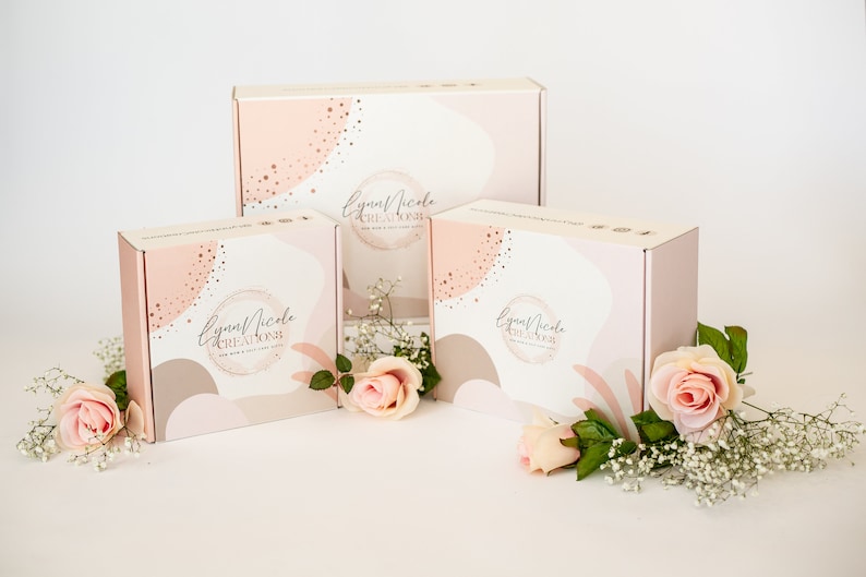May include: Three pink and white gift boxes with a gold and white abstract design. The boxes have the text "Lynn Nicole Creations" on them. The boxes are surrounded by pink roses and white baby's breath.
