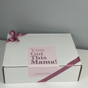 May include: A white rectangular cardboard shipping box wrapped with a mauve satin ribbon tied in a bow. A rectangular label on the lid features the text "You Got This Mama!" in dark purple, with "LynnNicole Creations" printed below.
